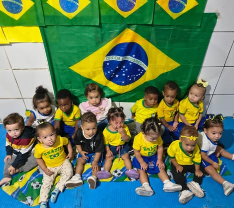 Bebês do berçário reunidos com a bandeira do Brasil